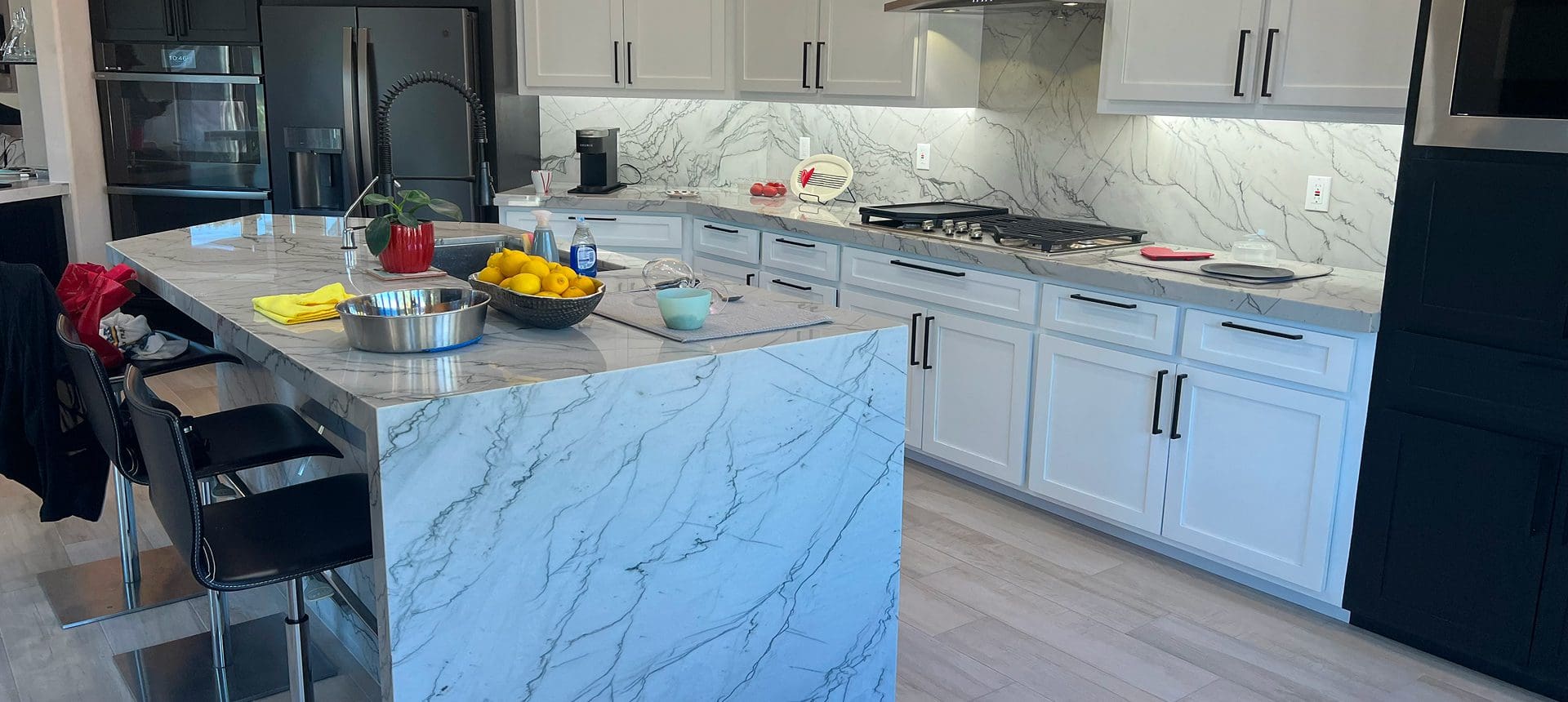 Modern kitchen with marble countertops and white cabinets.